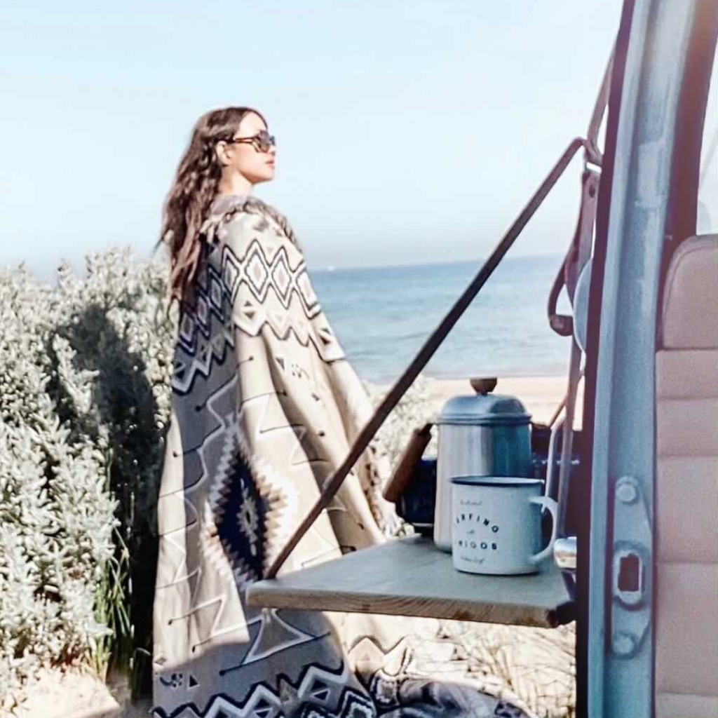 Woman standing near vehicle at beach wearing Hendeer Hey Jude Picnic Rug draped over her shoulder.