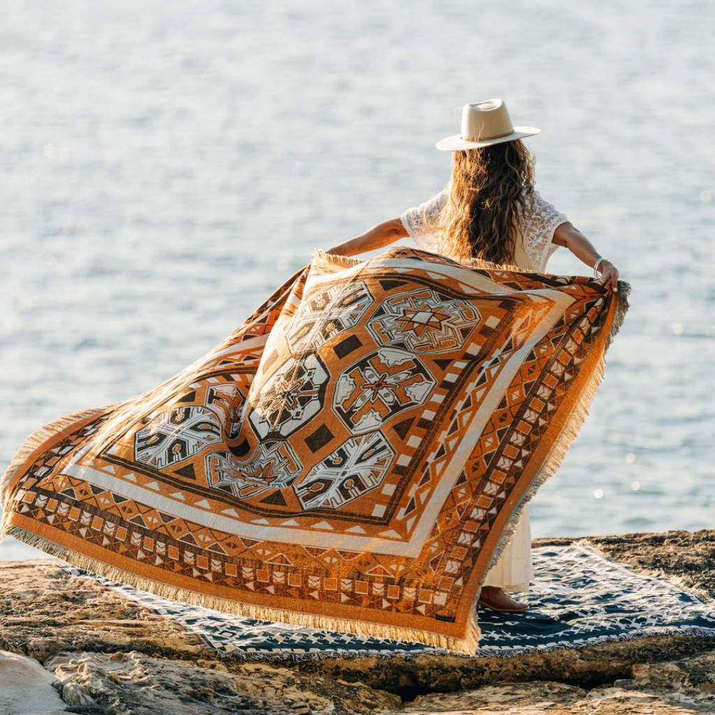 Woman at beach with Hendeer picnic rug floating behind her. Child of Nature pattern.