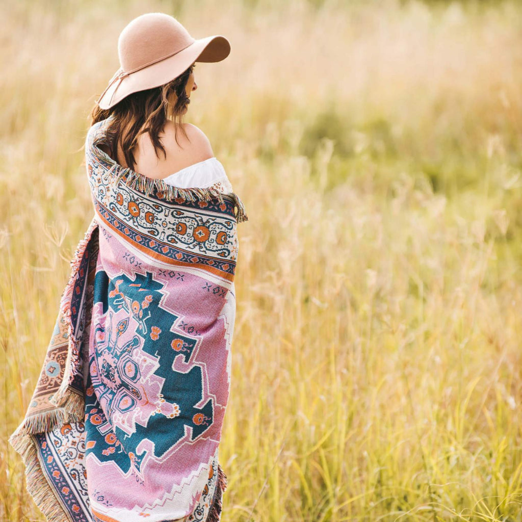 Woman standing in field with Hendeer Strawberry Fields picnic rug wrapped around her.